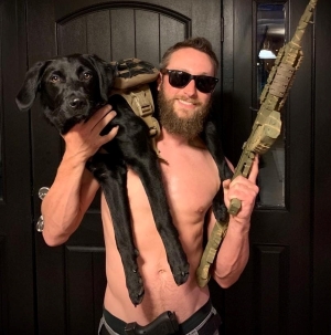 Joel holding an AK-47 with his dog Rio on his shoulder